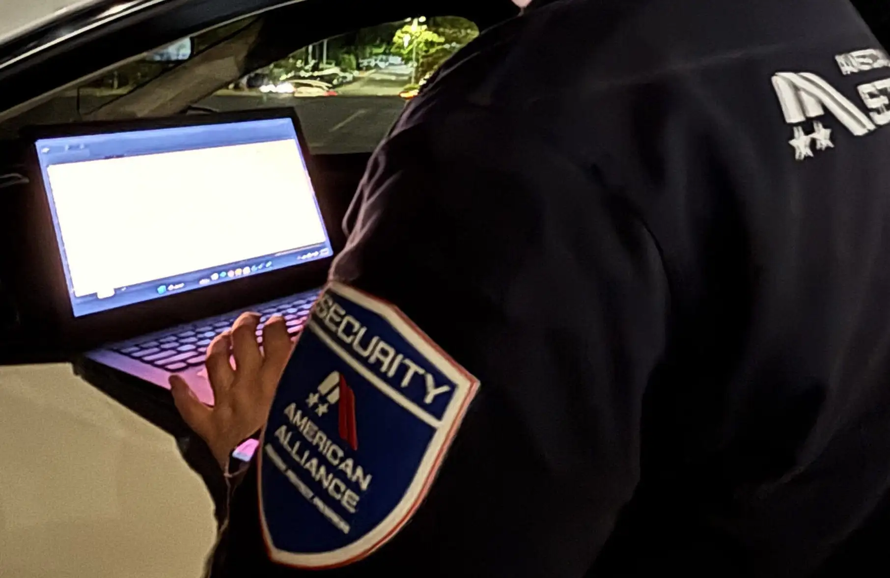 An American Alliance Security officer typing a patrol report on a laptop
