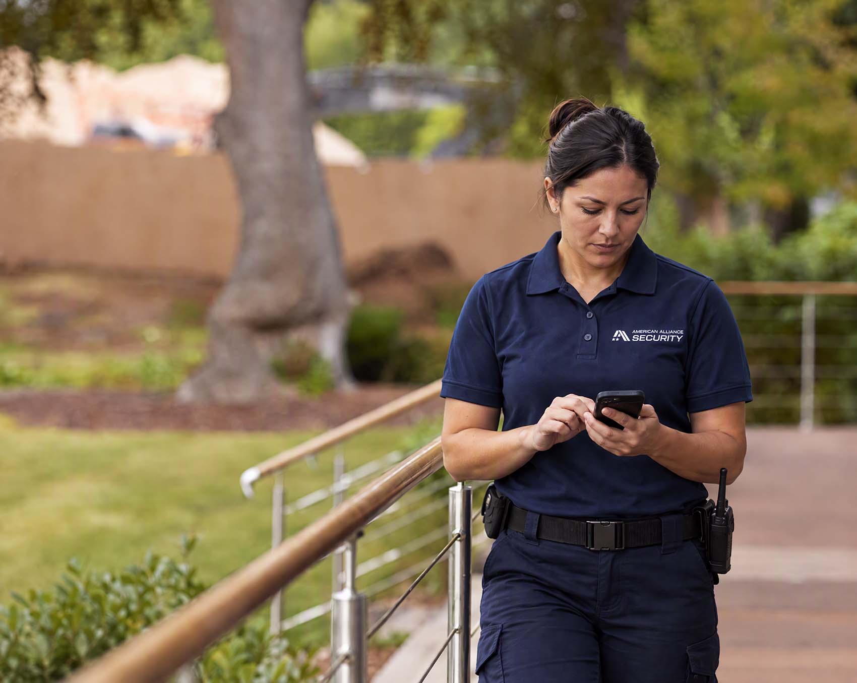 An American Alliance Security officer checking her phone on a landscaped walkway