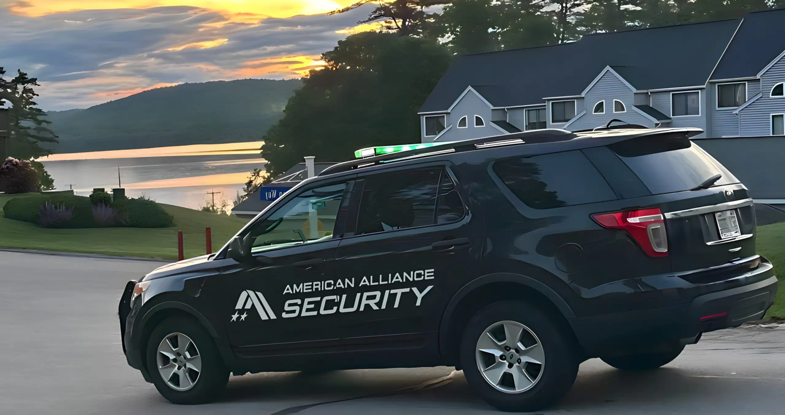A black American Alliance Security patrol vehicle with a roof light bar parked at dusk beside a lakeside property