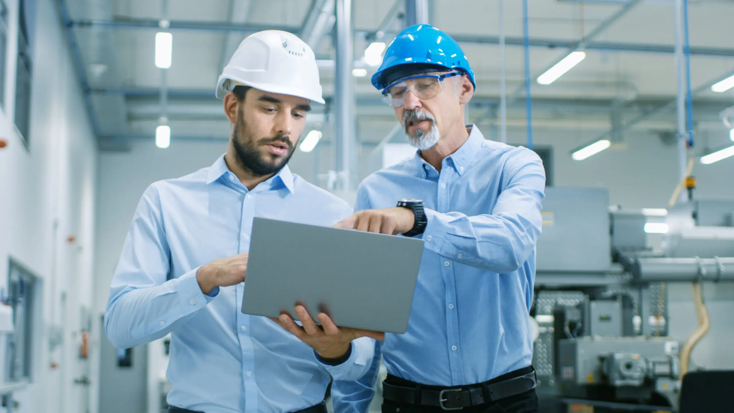 Two managers in hard hats reviewing a laptop on a factory floor
