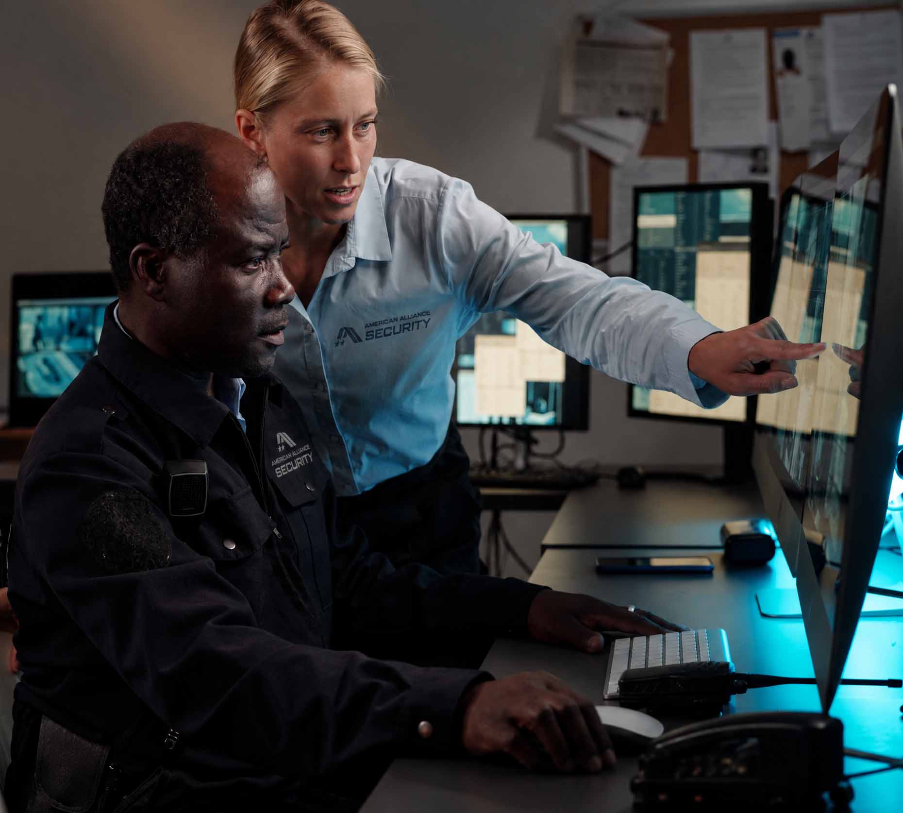 An American Alliance Security supervisor pointing out camera footage to a seated officer in a monitoring room