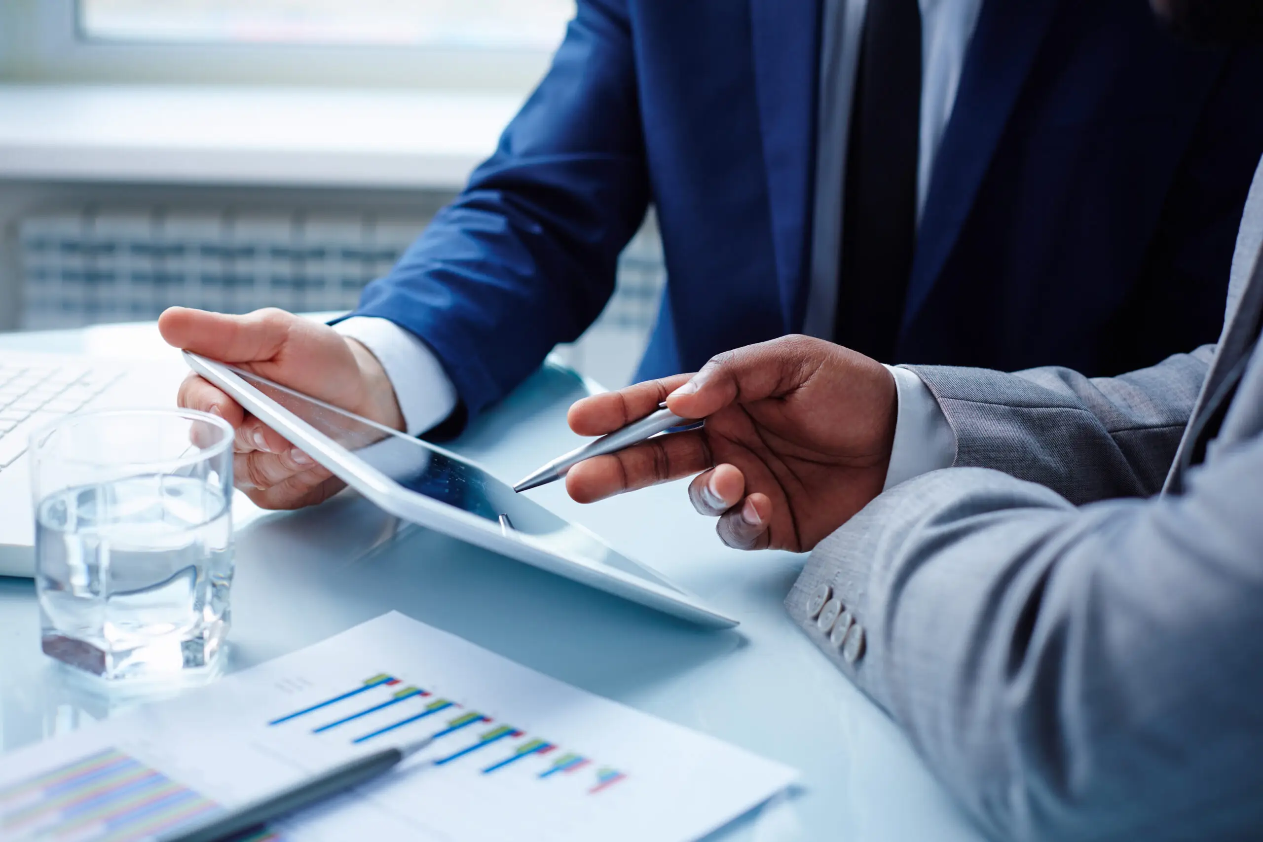 Two people in suits reviewing findings on a tablet at a meeting table