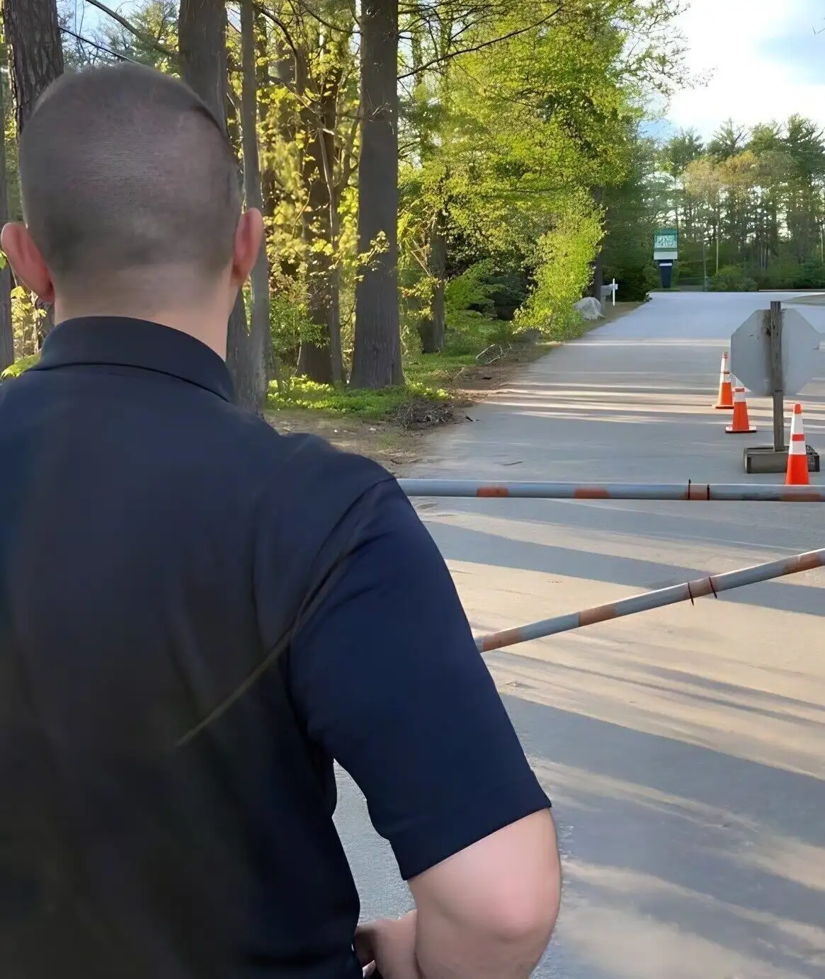 A security officer watching a gated entrance road from the checkpoint