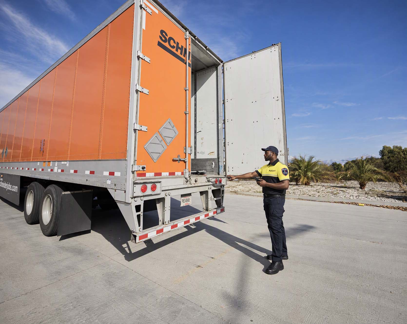 A security officer inspecting the open rear doors of a freight trailer in a distribution yard