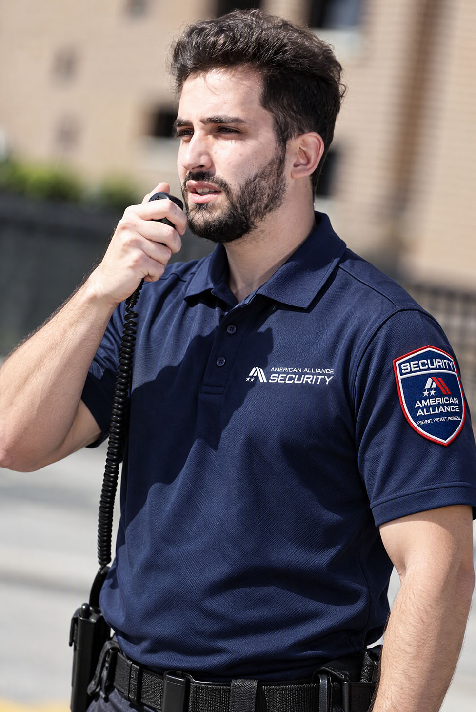 An American Alliance Security officer speaking into a shoulder radio outside a building