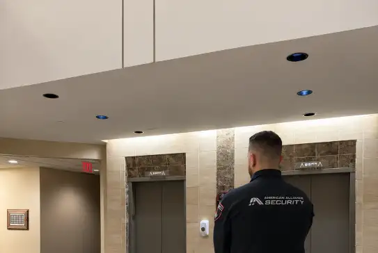An American Alliance Security officer standing watch by the elevators in a government building lobby